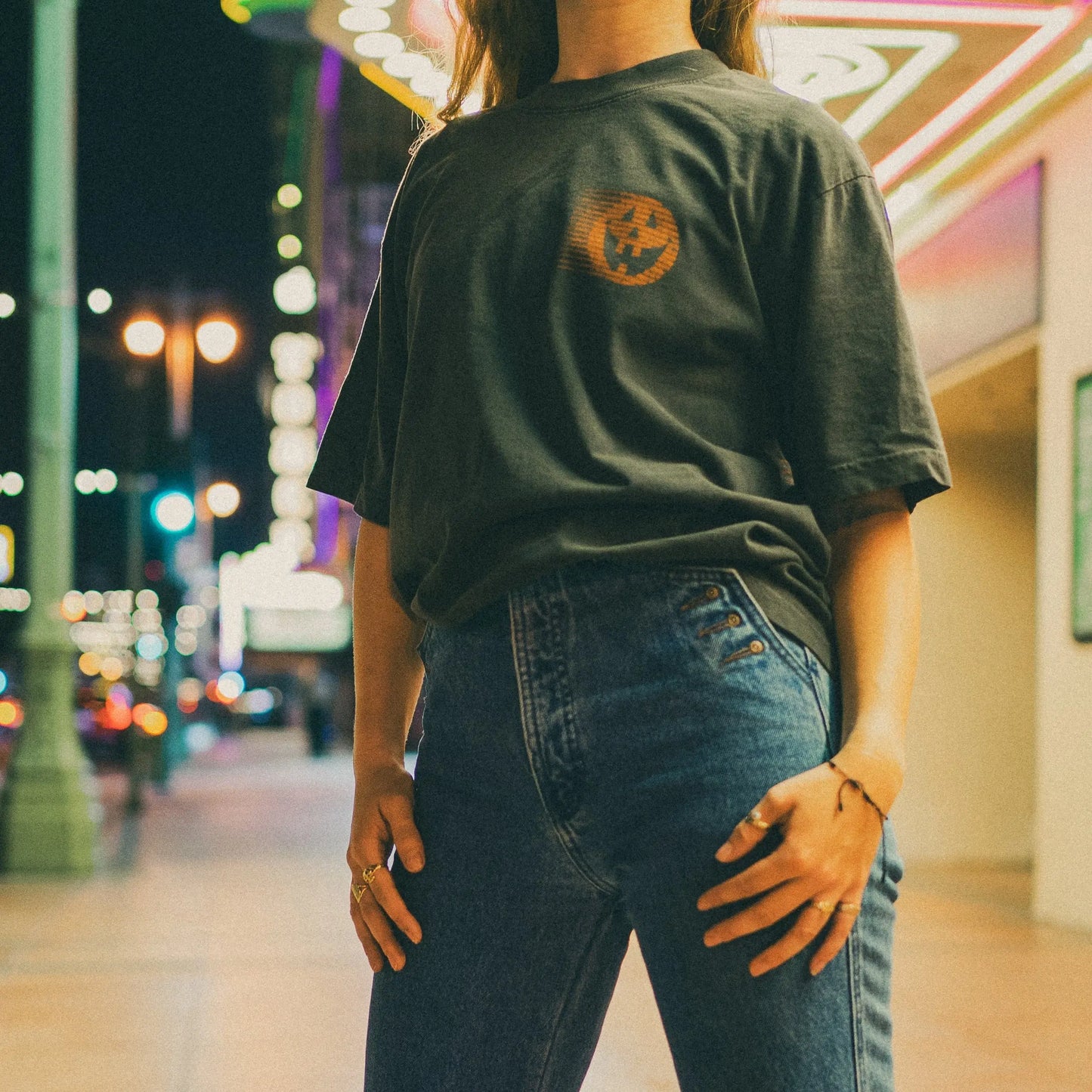 Person wearing a dark green t-shirt with a pumpkin design in an urban night setting.